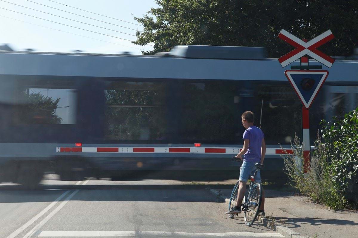 Tog passerer jernbaneoverskæring og en cyklist venter ved bommen